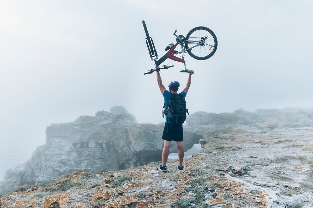man on a mountain triumphantly holding a bike over his head